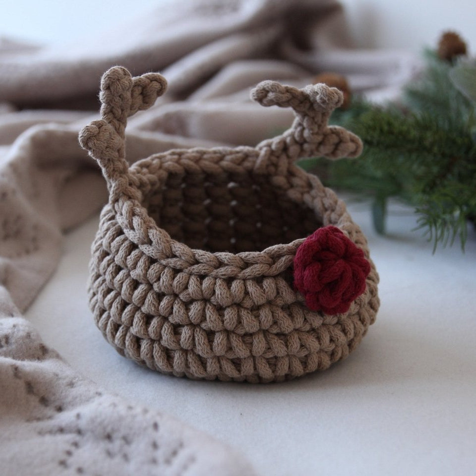Crocheted reindeer basket with antlers and a red nose on a soft surface with a blurred background
