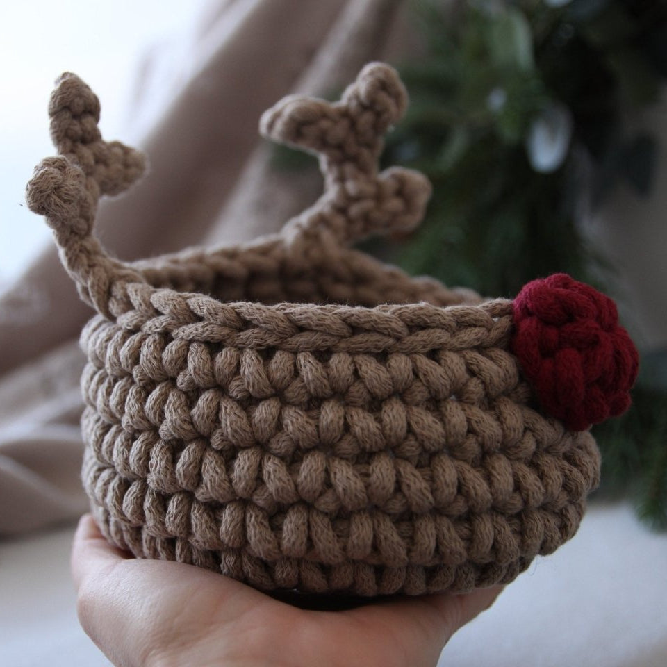 Handmade crochet basket with deer antlers and a red nose held in a hand.