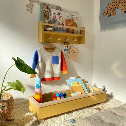 Children's play area with a wooden shelf, colorful sweater, and toys on a carpeted floor.