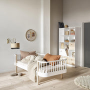 Bright and airy bedroom featuring an Oliver Furniture Wood Original Day Bed in White/Oak, styled with soft pillows and bedding, alongside a white shelving unit displaying decorative baskets and objects. 