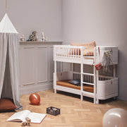 Oliver Furniture Wood Mini+ Low Bunk Bed in white creating a comfortable, space-saving, and stylish Scandinavian-inspired sleeping arrangement for children in a warmly lit room. 