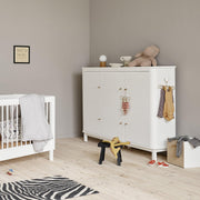 Oliver Furniture Wood Multi Cupboard with three white doors, soft-close function, leather handles, and hanging rail, displayed in a modern Scandinavian nursery room with a crib and storage bench.